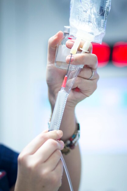 Foto manos cortadas de un médico inyectando una jeringa en un goteo intravenoso en un hospital