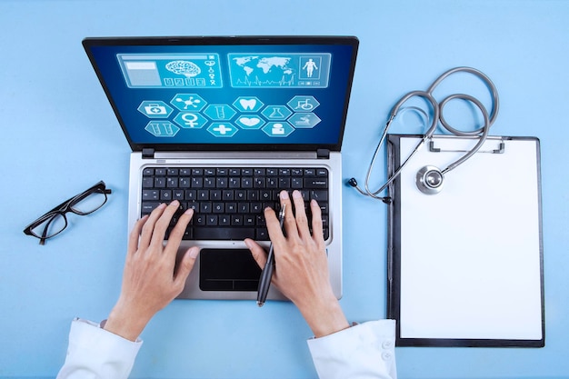 Foto manos cortadas de un médico usando una computadora portátil sobre un fondo azul