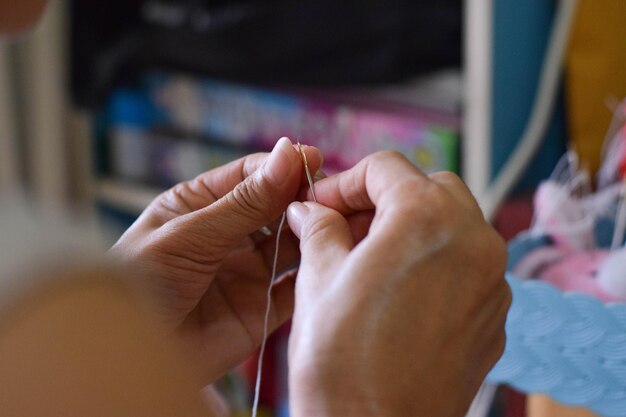 Manos cortadas de una mujer con aguja de coser y hilo