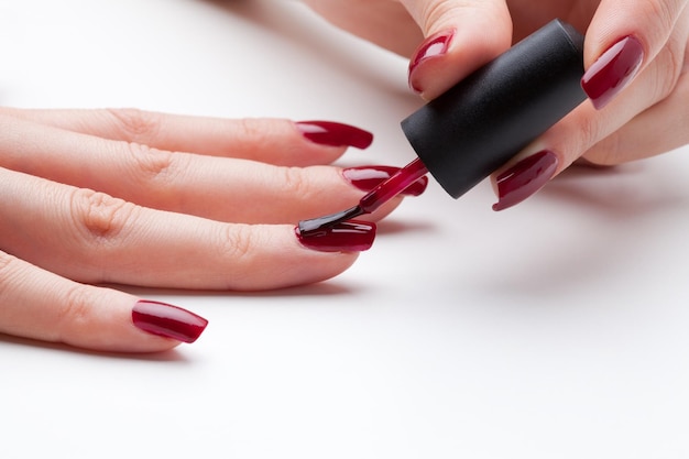 Manos cortadas de una mujer aplicando esmalte de uñas contra un fondo blanco