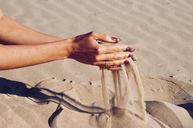 Foto manos cortadas de una mujer derramando arena en la playa