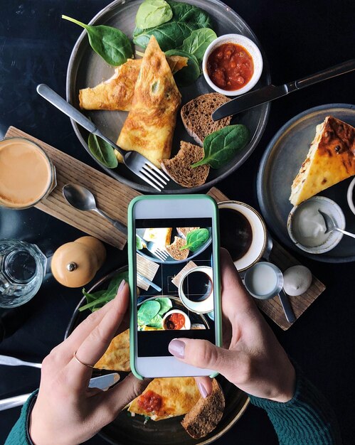 Foto manos cortadas de una mujer fotografiando comida con un teléfono inteligente en la mesa