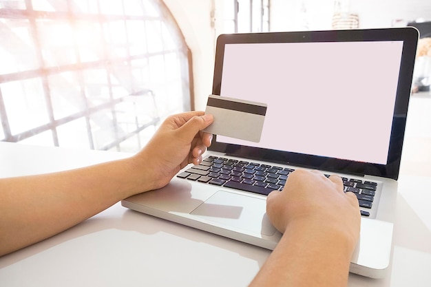 Manos cortadas de una mujer haciendo un pago con tarjeta mientras usa una computadora portátil en la mesa