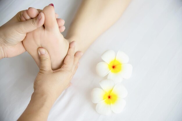 Manos cortadas de una mujer masajeando los pies de un cliente con flores en un spa