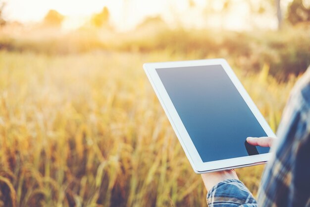 Foto manos cortadas de una mujer sosteniendo una tableta digital contra plantas en una granja