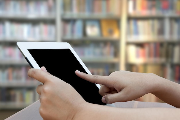 Manos cortadas de una mujer usando una tableta digital en la biblioteca