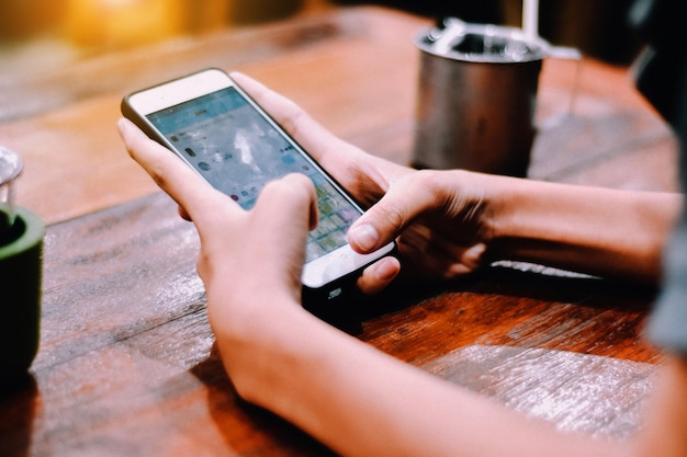 Manos cortadas de una mujer usando un teléfono en la mesa.