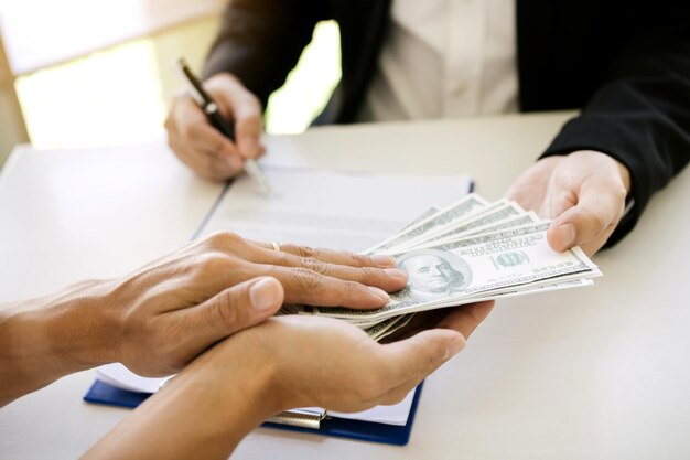 Foto manos cortadas de una persona que da soborno a una persona de negocios firmando papeles en la mesa