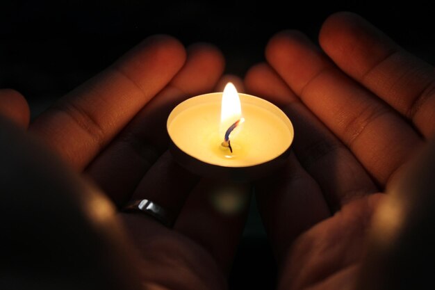 Manos cortadas de una persona que sostiene una vela encendida