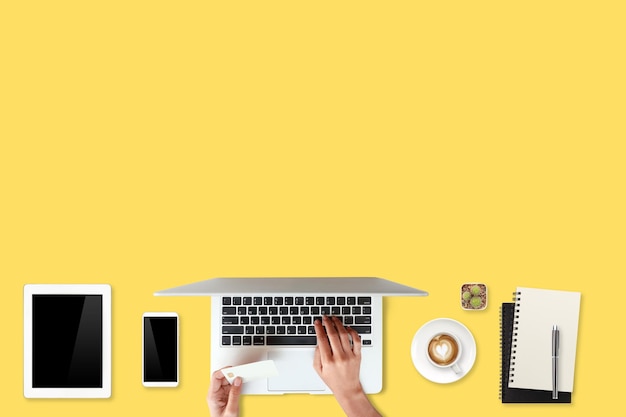 Manos cortadas de una persona que usa una computadora portátil contra un fondo amarillo