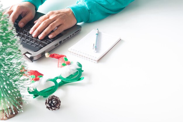 Manos cortadas de una persona que usa una computadora portátil con decoraciones navideñas en la mesa en casa