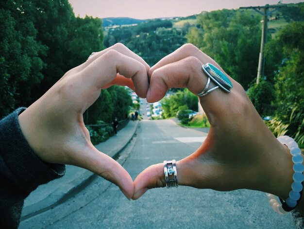 Manos cortadas de personas haciendo forma de corazón contra los árboles