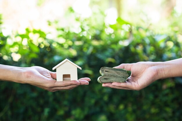 Foto manos cortadas de personas sosteniendo casas modelo y dinero contra plantas