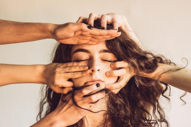 Manos cortadas de personas sosteniendo a la mujer cara contra la pared