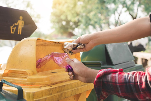 Foto manos cortadas poniendo botellas de agua de plástico en el contenedor de basura en un parque público