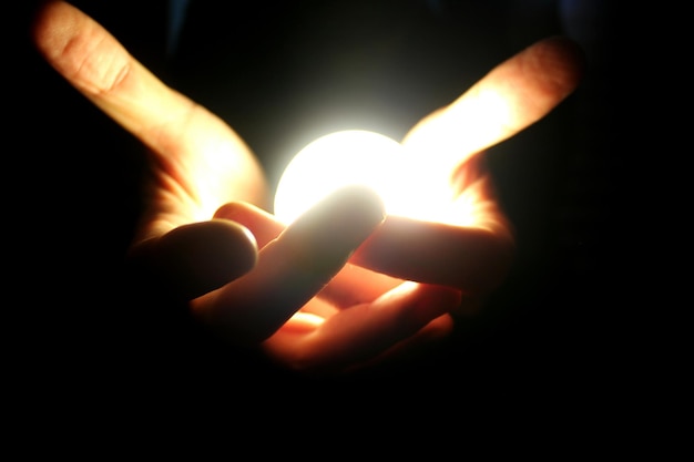 Foto manos cortadas sosteniendo una bombilla iluminada sobre un fondo negro