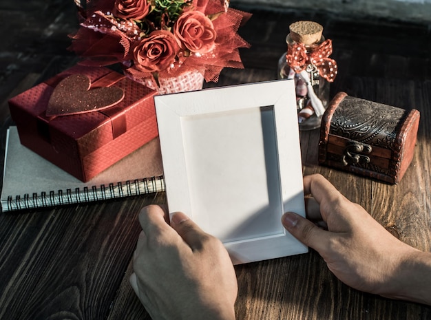 Manos cortadas sosteniendo un marco de fotos vacío y un regalo