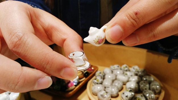 Manos cortadas sosteniendo una taza de té pequeña y una tetera