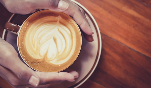 Manos cortadas tocando la taza de café en la mesa
