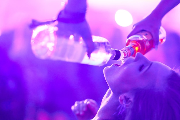 Manos cortadas vertiendo alcohol en la boca de una amiga durante una fiesta por la noche