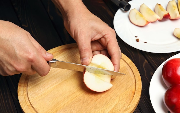 Foto manos cortan la jugosa manzana roja con un cuchillo en la tabla de cortar, cocinar manzanas sin núcleos para el postre