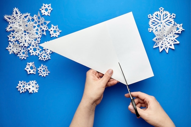 Manos cortando una hoja de papel blanco para hacer copos de nieve