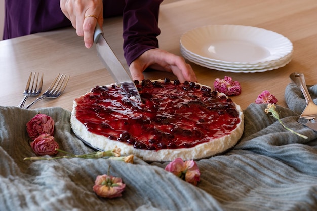 Foto manos cortando pastel de queso en fondo de madera con rosas alrededor