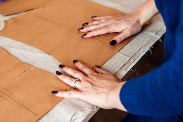 Las manos de la costurera sostienen el patrón en la tela el diseñador prepara el patrón