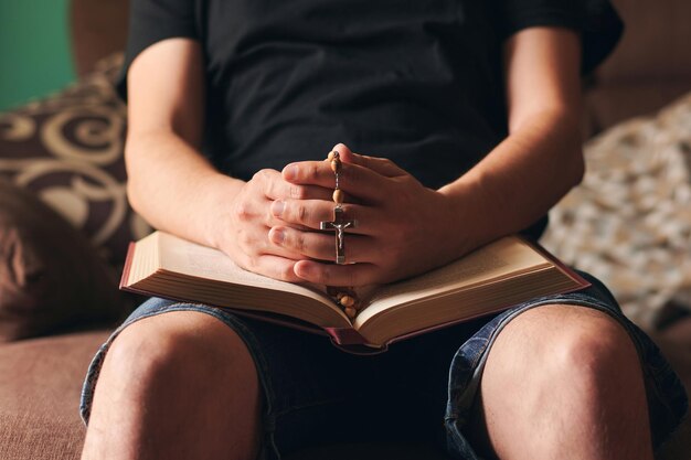 Manos de un creyente con una biblia santa y una cruz en sus manos