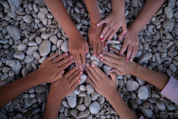 Manos de cuatro niños haciendo un círculo en una playa de guijarros