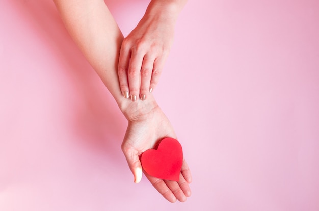 Las manos de una dama sosteniendo un corazón en una pared rosa, el día de San Valentín