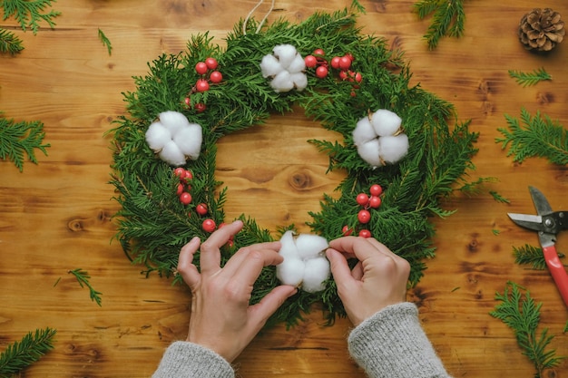 Manos decorando la corona de Navidad de hoja perenne de bricolaje con bola de algodón