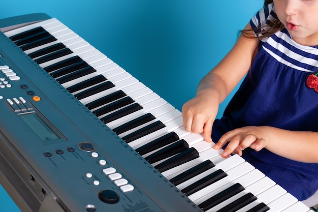 Manos y dedos de una niña niño presionando las teclas de un piano electrónico, lección de música