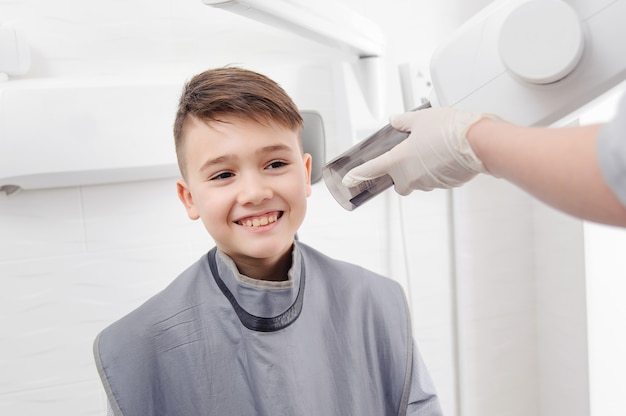Las manos del dentista hacen una imagen de rayos x de la mandíbula para el niño en la clínica dental
