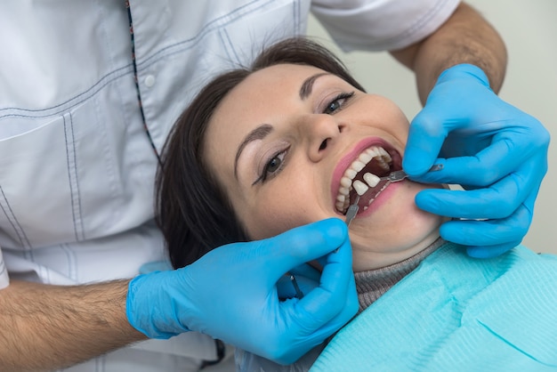 Manos del dentista con muestra de dientes y paciente