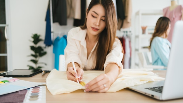 Manos de diseñadora de moda femenina o sastre mano midiendo papel con cinta métrica para hacer patrones de ropa Diseñadora de moda a medida en el taller trabajando para una nueva colección Enfoque en las manos