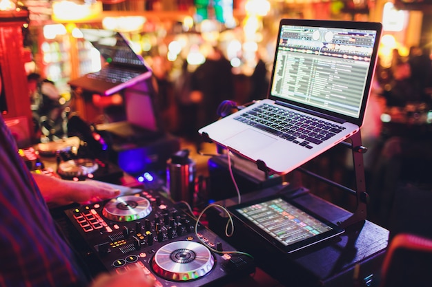 Manos de DJ mezclan pistas en un tocadiscos digital y software en una computadora portátil con software de mezcla profesional