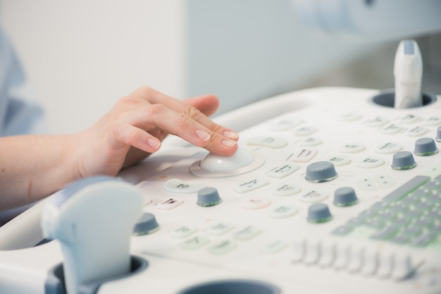 Las manos del doctor de la mujer joven se cierran para arriba preparándose para una exploración del dispositivo de ultrasonido.