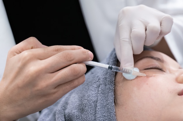 Las manos de los doctores que hacen una inyección cosmética en cara de la mujer joven. Tratamiento de belleza.