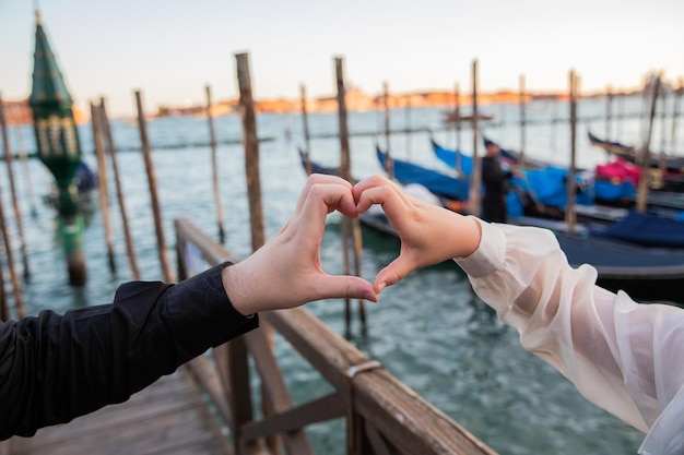 Las manos de dos amantes forman un corazón en las góndolas de Venecia en el concepto de fondo del romance y el amor