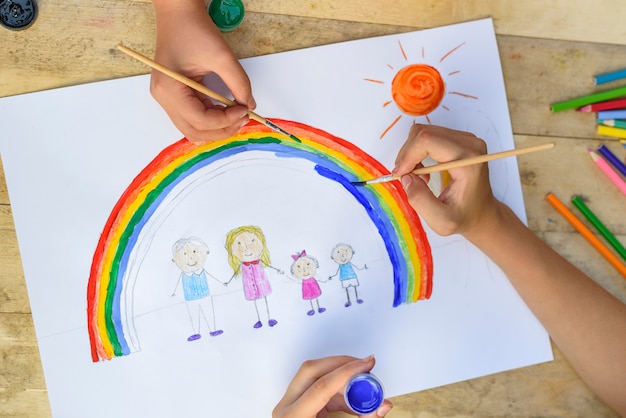 Las manos de dos niños dibujan un dibujo con pincel y pinturas. Vista superior