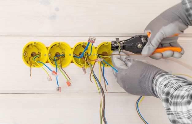 Manos de electricista instalando toma de corriente con destornillador en la pared de la nueva casa de madera