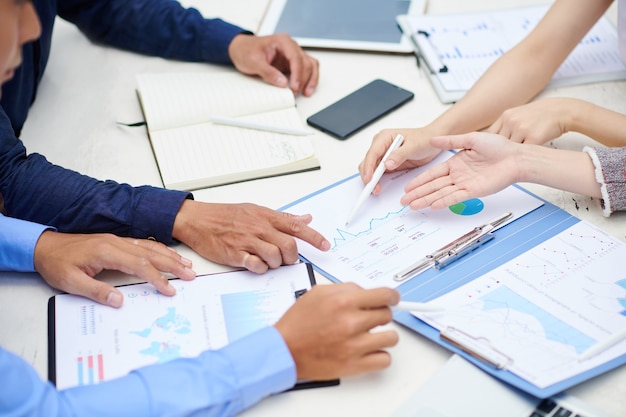 Manos de empresarios apuntando al gráfico en el informe financiero sobre la mesa y discutiendo el desarrollo de la empresa