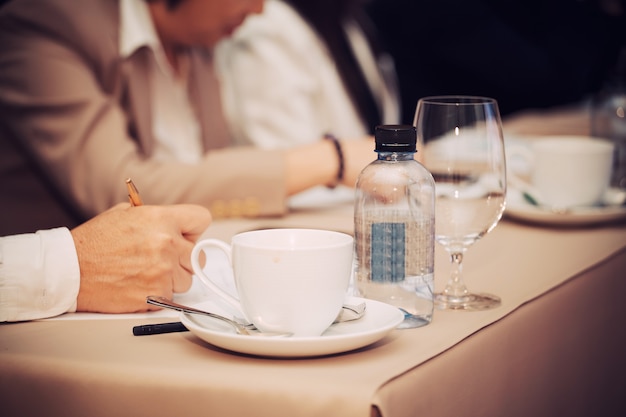 Manos de empresarios con bolígrafo o lápiz, papeles y tazas de café en la sala de seminarios