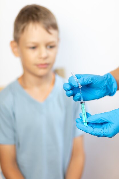 las manos de la enfermera con guantes azules abren la caja con la jeringa frente a la cara del niño