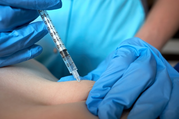 Foto manos de enfermera en guantes quirúrgicos azules haciendo inyección de anticoagulante por vía subcutánea al niño. vista de cerca