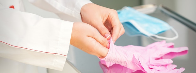 Manos de la enfermera poniéndose guantes protectores esterilizados rosa en el laboratorio