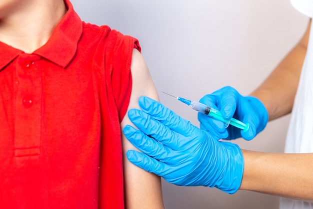 Las manos de las enfermeras en guantes azules inyectan la vacuna a través de una jeringa en el hombro de los niños