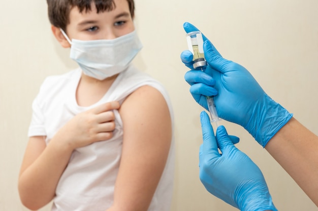 Manos de enfermeras en guantes azules preparando una vacuna para un niño