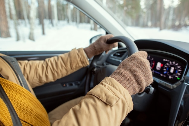 Manos enguantadas de joven hombre activo contemporáneo en ropa de invierno abrigada sosteniendo por dirección mientras está sentado en el automóvil y conduciendo durante el viaje